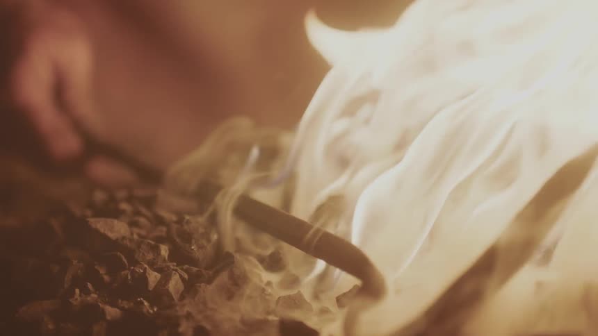 Someone holding a poker in a campfire and turning it