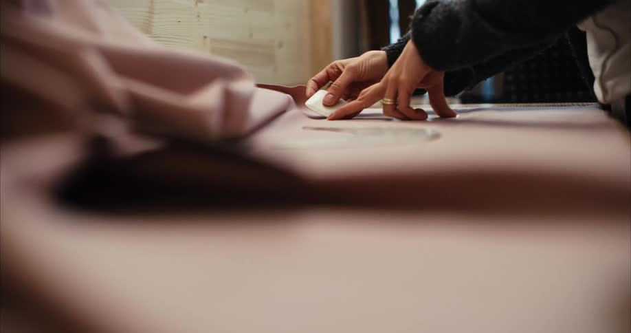 A woman uses a pattern and tailors chalk to mark fabric for cutting