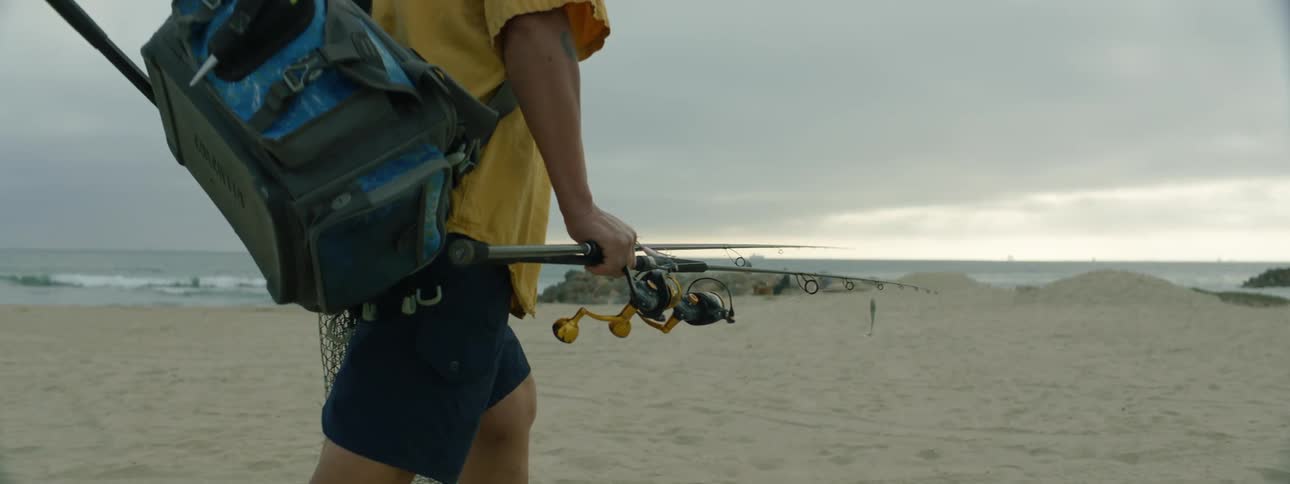 A man is walking in the sand with a fishing pole