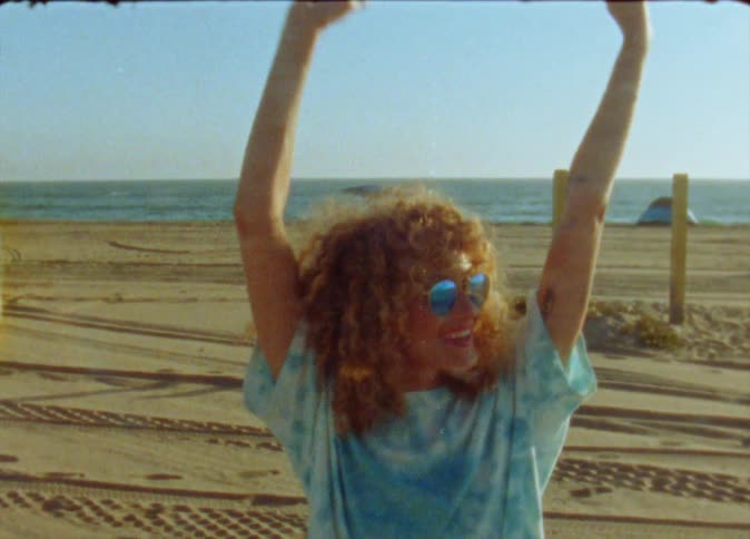 A woman throws her arms up and dances on the beach