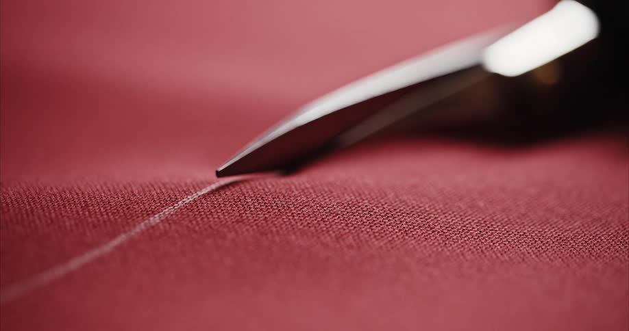 The red fabric is being cut with a scissor