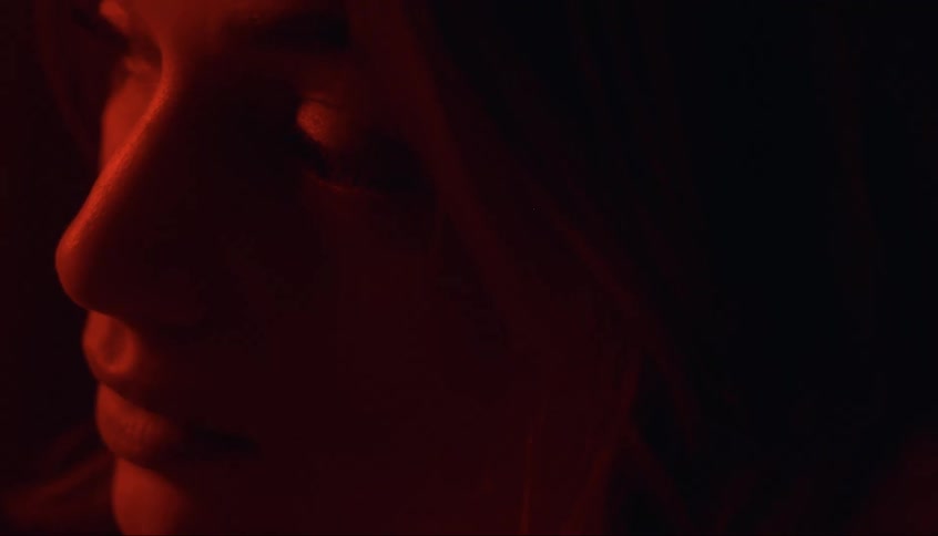A woman bathed in a soft red glow holding a flower in her hand