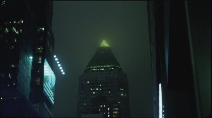 A tower with lights on is seen between buildings in a hazy downtown night sky