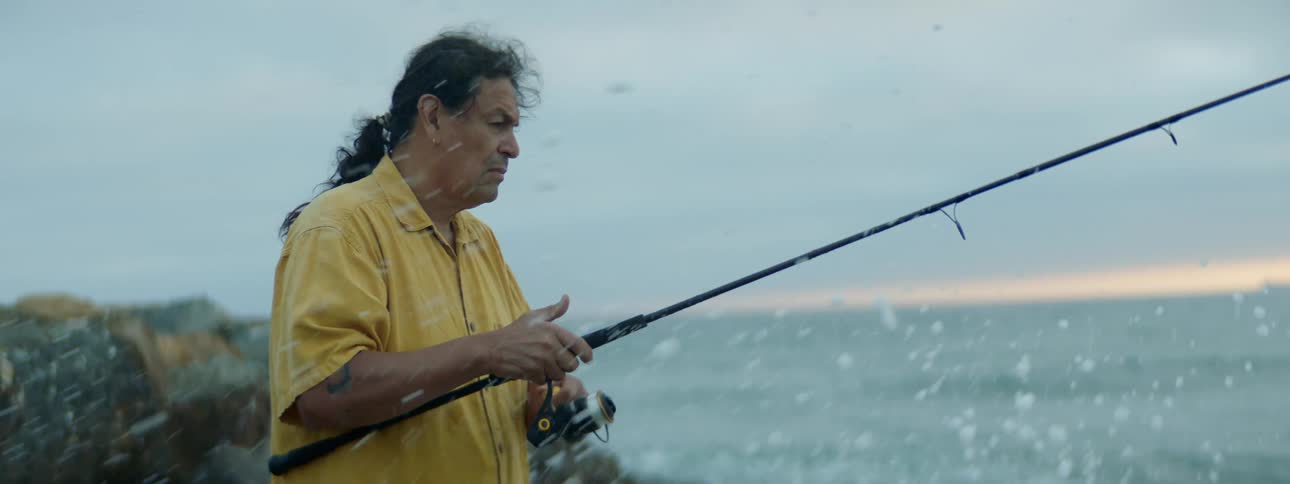 Man fishing on shore lets out line as water splashes