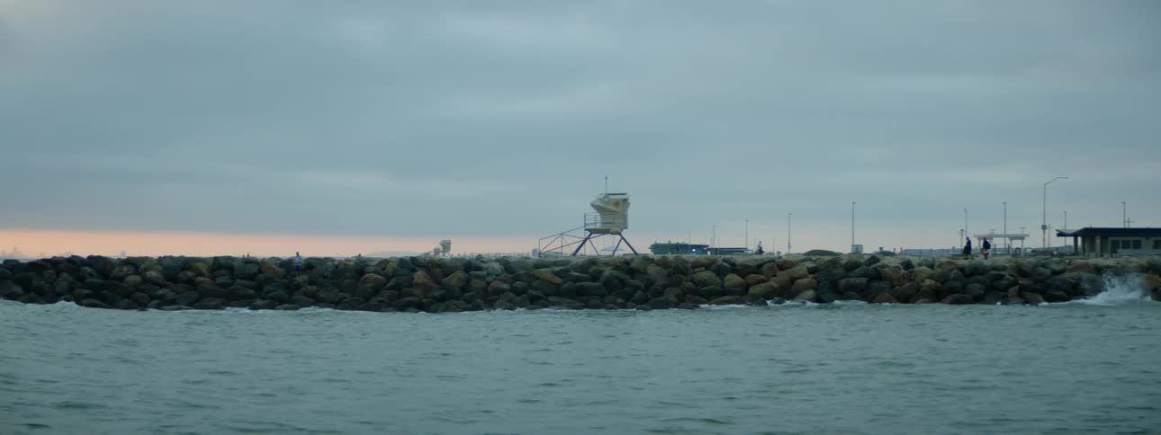 People move along breakwater near the marina under an overcast sky