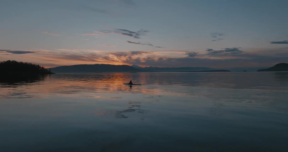A person kayaks in a lake as the sun sets