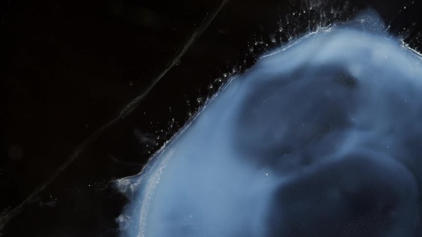 Blue gray blob expands in pale blue mixture that sends tendrils out into dark fluid