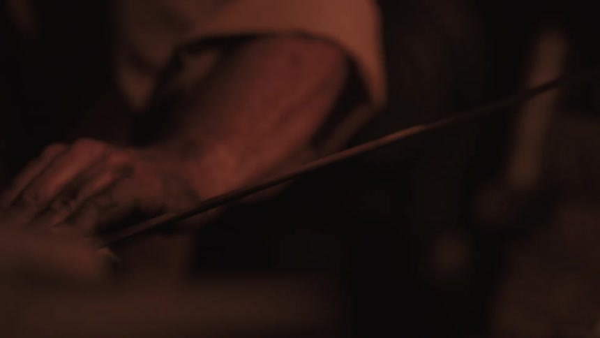 A man polishes a sword in a dark area