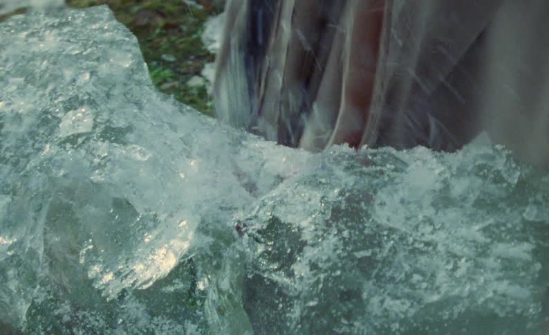 A young woman uses a large knife to chip away at a large block of ice outside