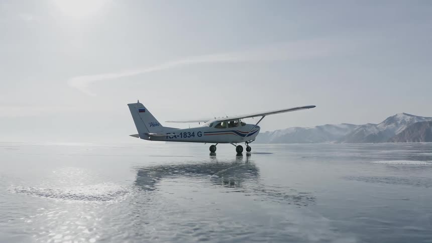 Cessna aircraft takes off from the surface of a frozen lake next to the mountains