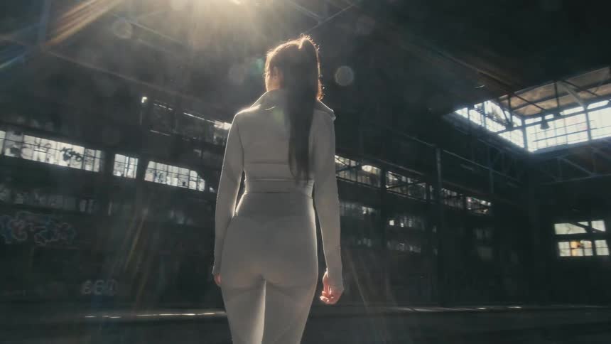 A woman stands and looks around while in an empty warehouse