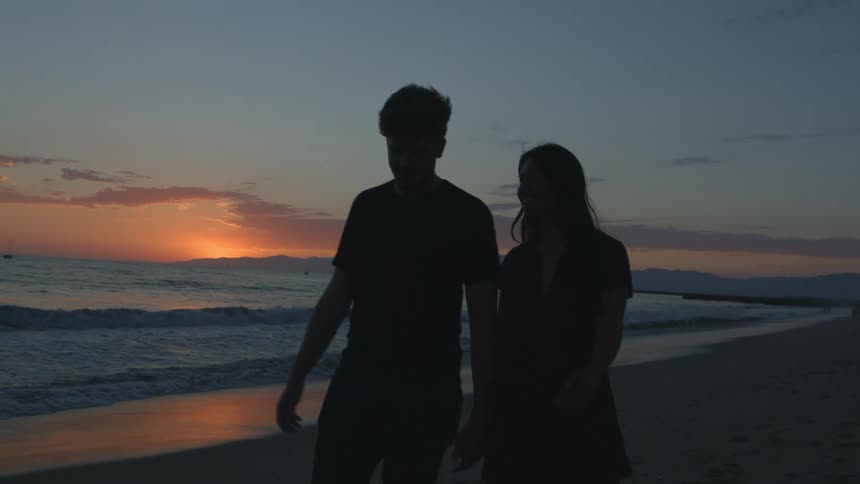 Man and woman are walking on the beach together at dusk