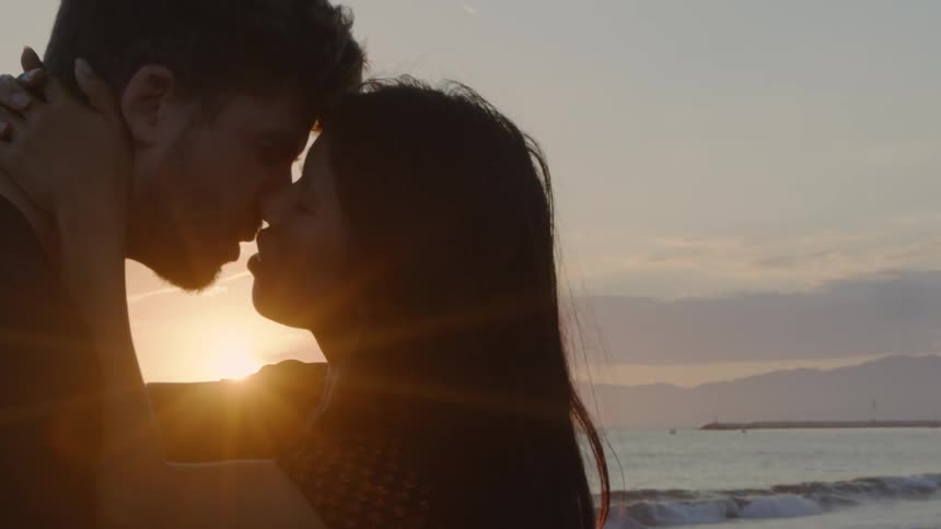 A couple is kissing at the beach as the sun is setting