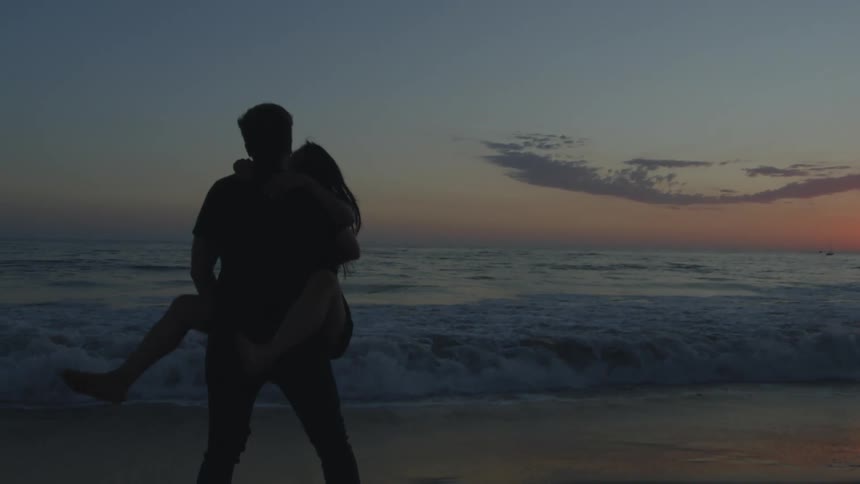 A woman runs along a beach and jumps into the embrace of a man at sunset