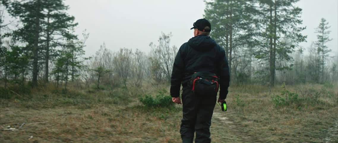A man carrying a fishing rod walks through the wilderness on a cloudy evening