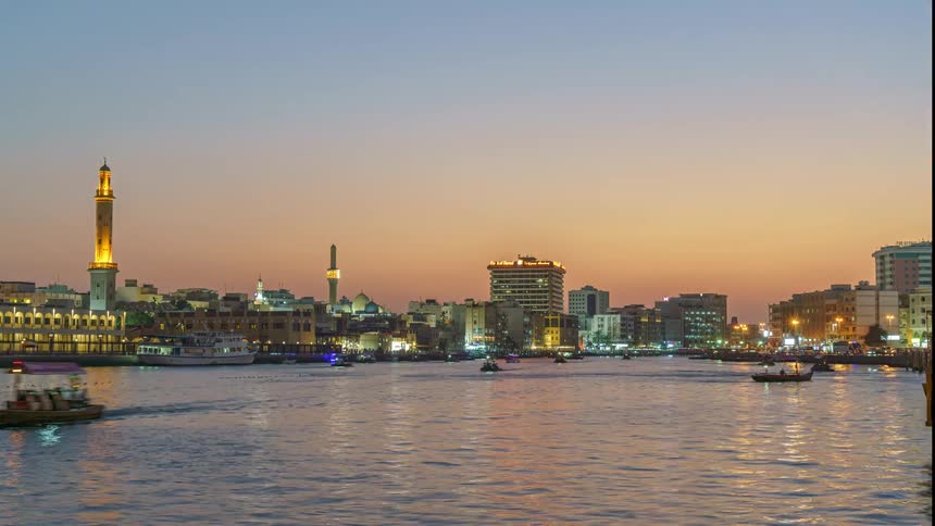 Boats travel along a large waterway in a metropolis at sunset