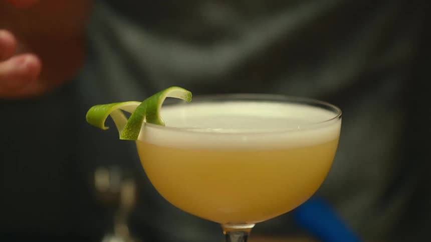 A person putting lime zest on an alcoholic beverage