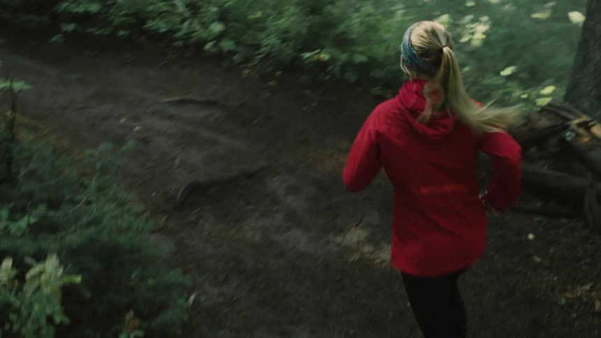 Woman jogs up slope following trail through woods