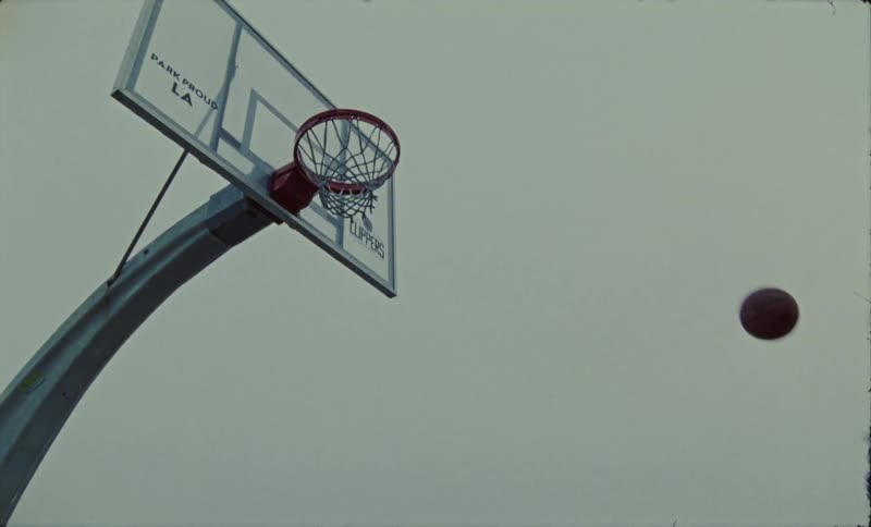 Male basketball player jumps and dunks basketball outdoors under an overcast sky