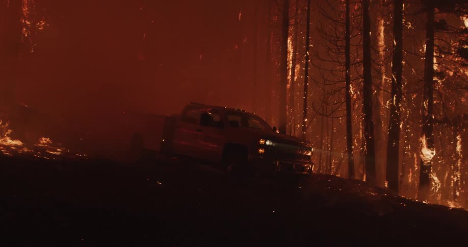 The silhouette of a firefighter running back to his pickup while forest trees are engulfed in flames