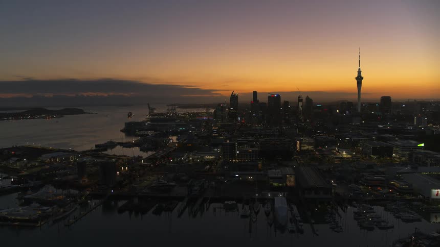 A tower and spire stand tall in a downtown skyline along the coast under an orange sunset sky