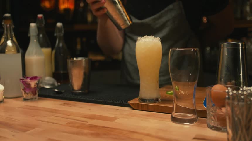 A bartender pours a cocktail in a glass and reaches for a flower to garnish it with