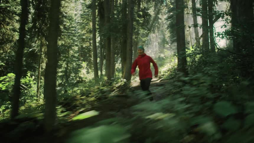 A woman is jogging on a trail in the forest on a mountain