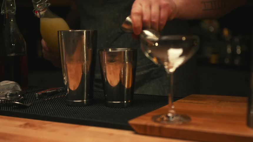 Bartender prepares mixed drink using metal shaker