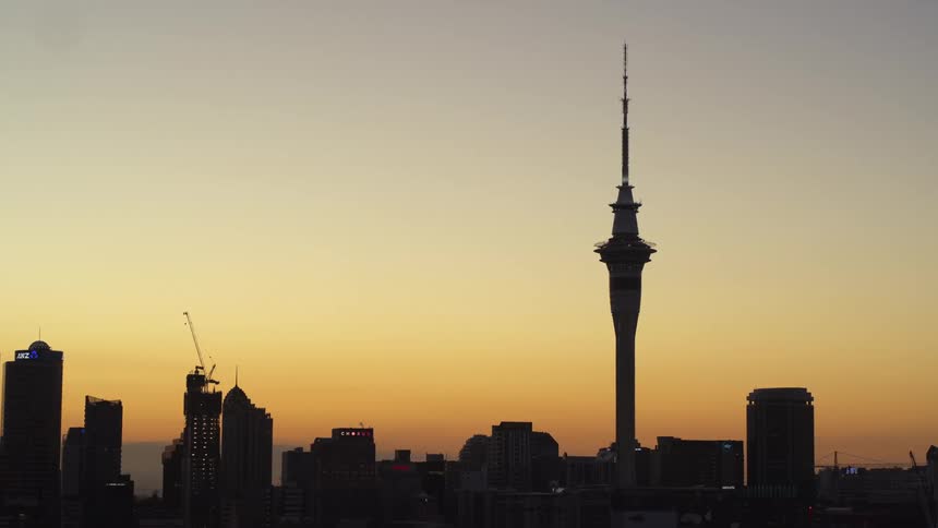 A spire stands tall in a silhouette of tall city buildings under an orange sky