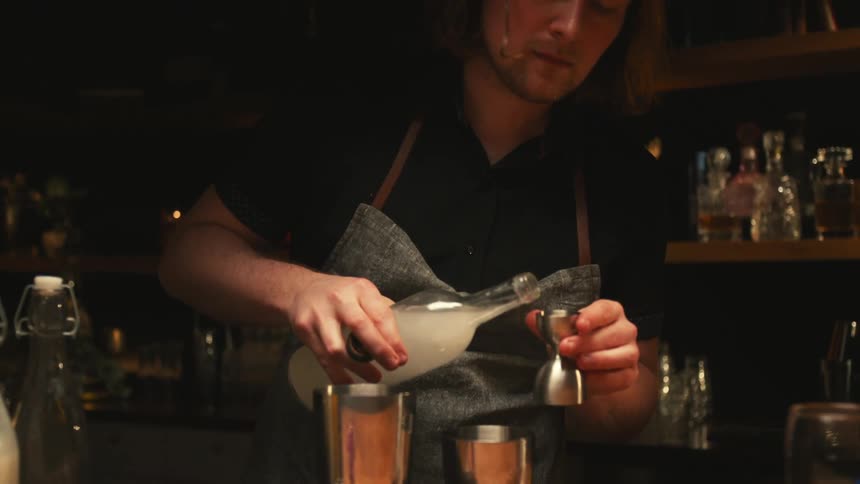 A bartender pours liquor into a shot glass