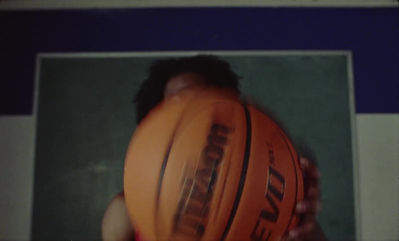 A man palming a basketball holding it in front of his face brings his hand down