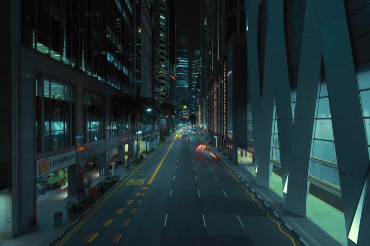 Cars traveling on an urban street between skyscrapers at night
