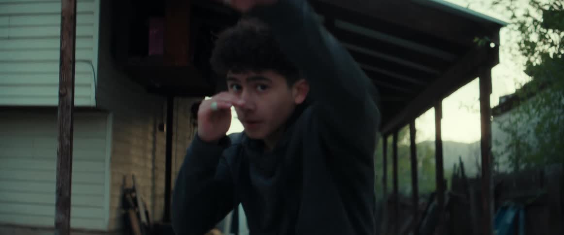 A teenage boy is outside in his yard practicing shadow boxing moves