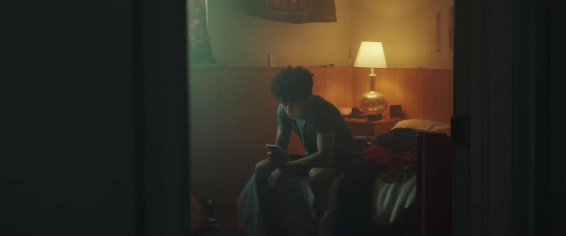 A young man looks at his smartphone while sitting on a bed in a bedroom during the day