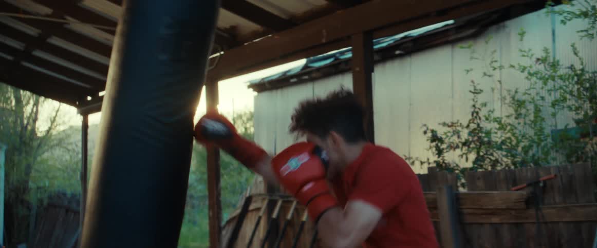 A young man hits a hanging heavy bag wearing boxing gloves in his yard