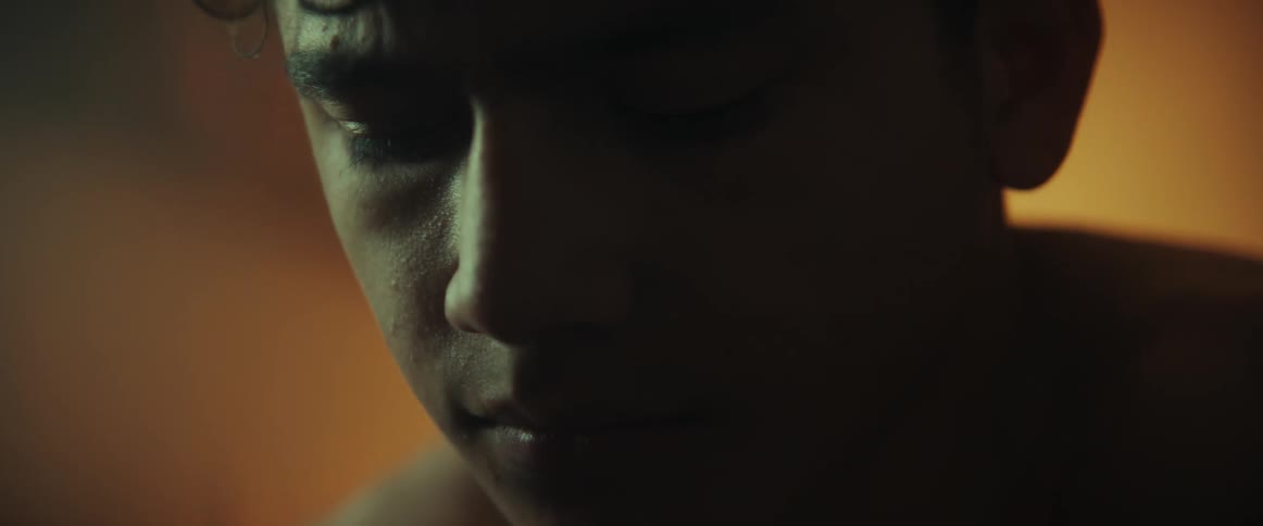 Close up of the face of a young shirtless teenager sitting in his bedroom