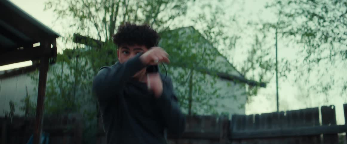Boy with gray hoodie and curly hair does boxing in the garden