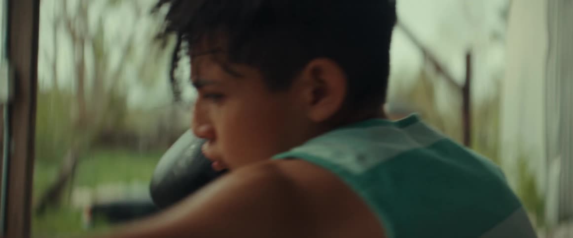 A boy wearing boxing gloves is on his patio hitting a punching bag