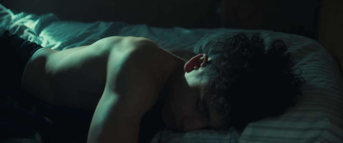 Shirtless young man trying to sleep on his bedroom at night tossing and turning on the bed