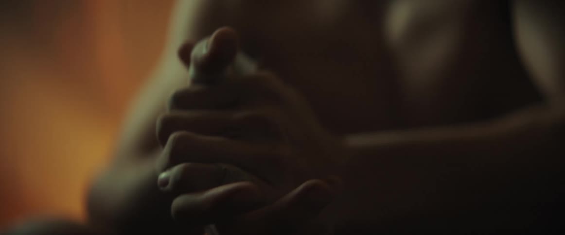 Young shirtless boxer sitting on a dimly lit room wraps his thumb with a bandage