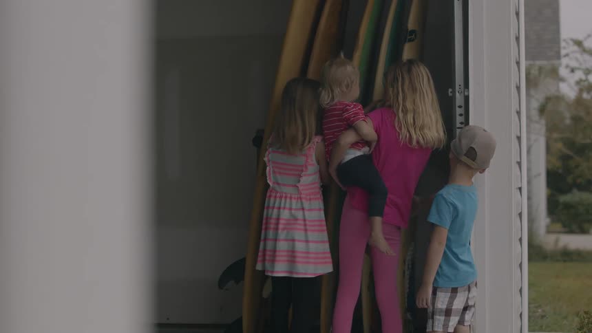 A group of children examine a group of surfboards stored in a garage