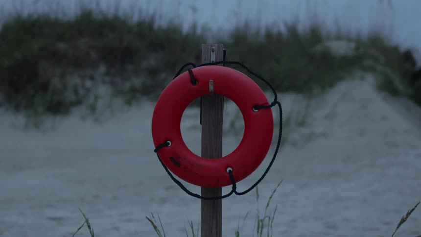 Bright red lifesaver hanging from a pole erected on the white sand of a beach at evening
