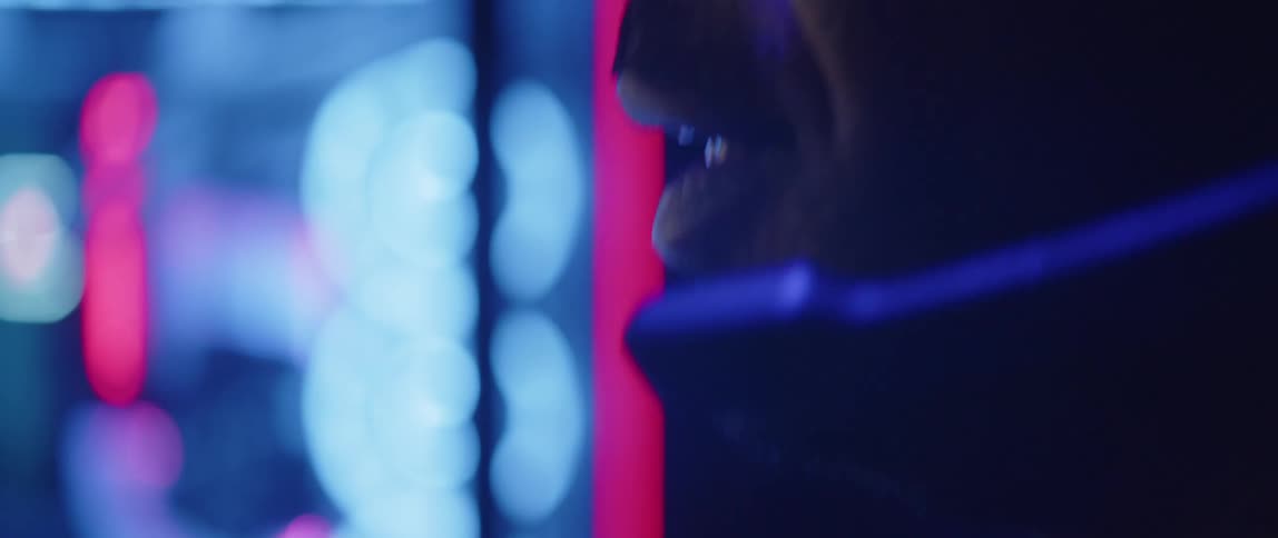 A man is speaking into a microphone on his headset as lights glow in the distance