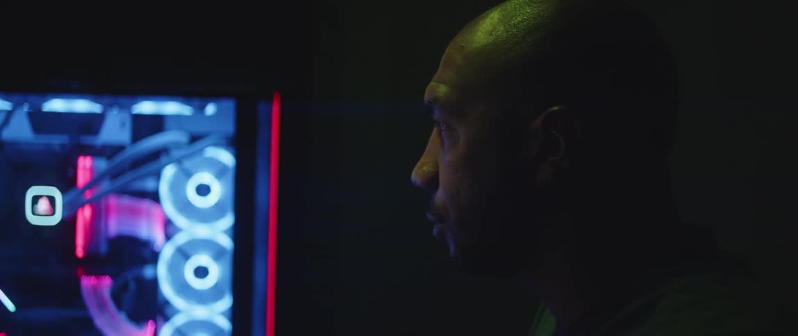 Colored lighting reflects off mans skin as he works with image on large display