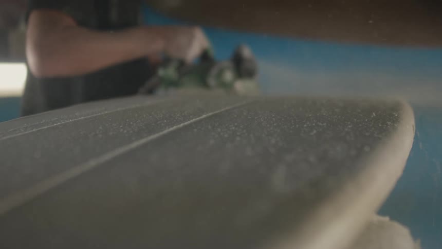 A man is moving a power sander across a piece of wood as sawdust flies