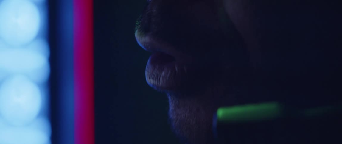 A man is speaking into a microphone on his headset as lights glow in the distance