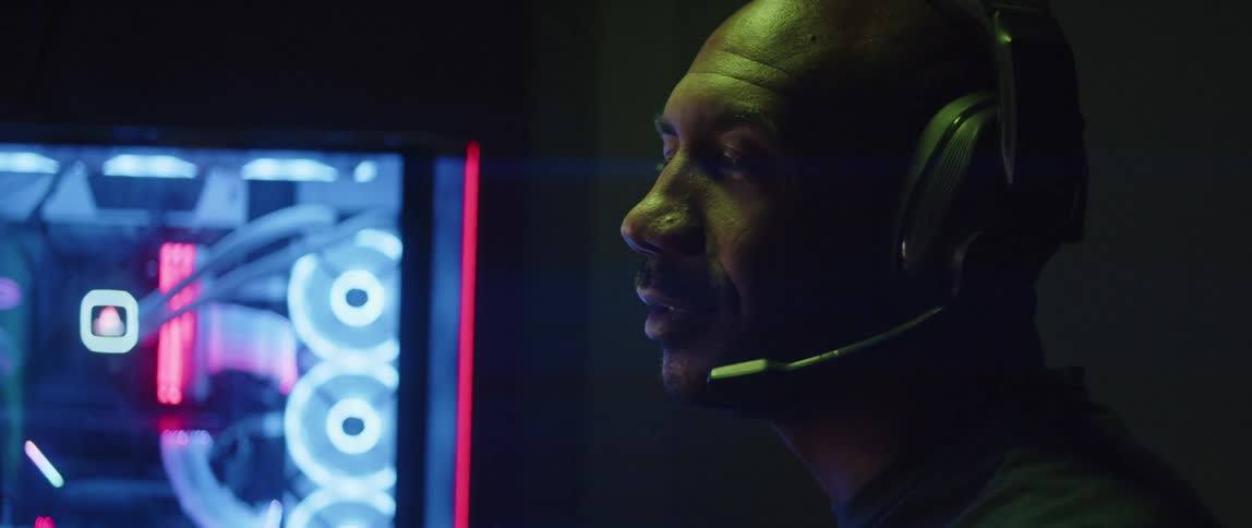 Close up of a man sitting in front of a computer under bright colorful rgb lights talking on a headset