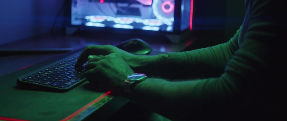 A man types on a computer keyboard as the lights inside his computer glow in the darkness