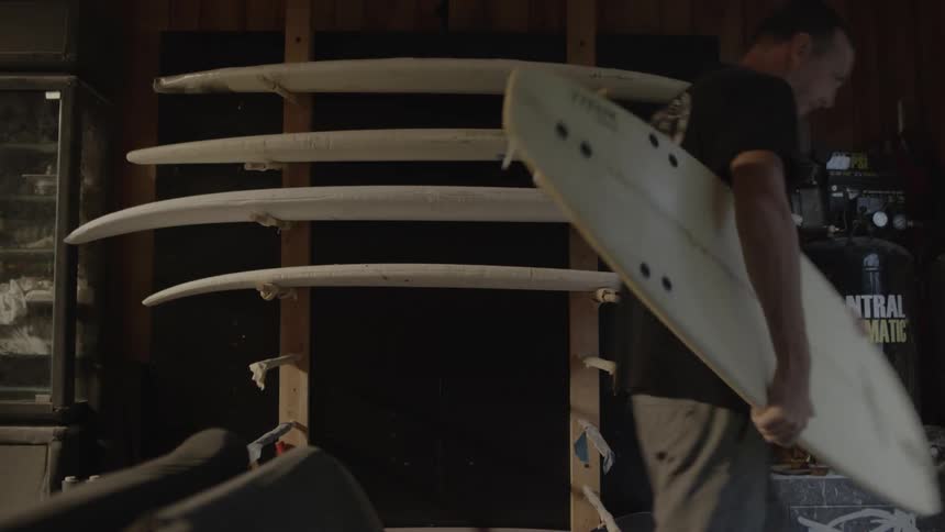 A man removes a surfboard from a wall display