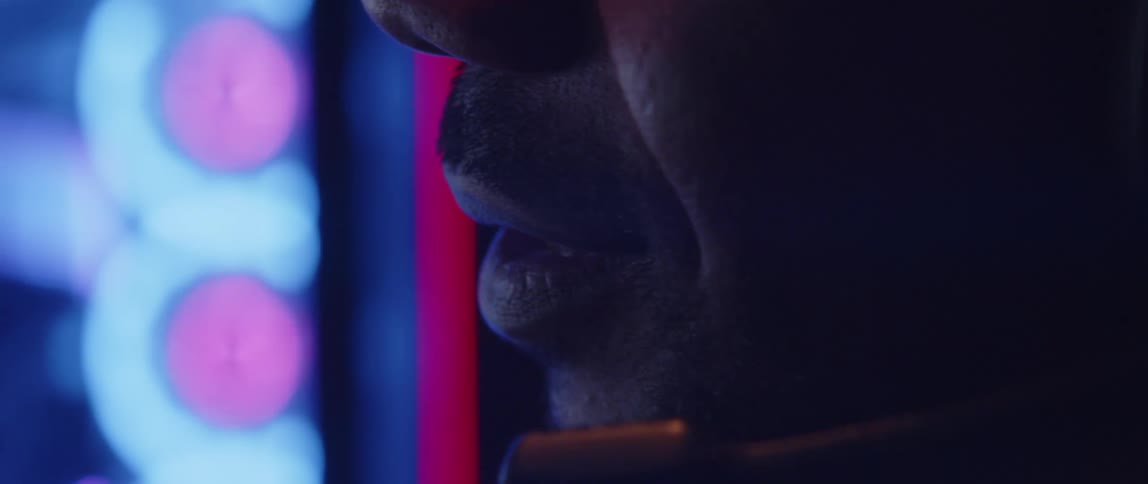 Man wearing a headset talks in a dim room near a digital monitor